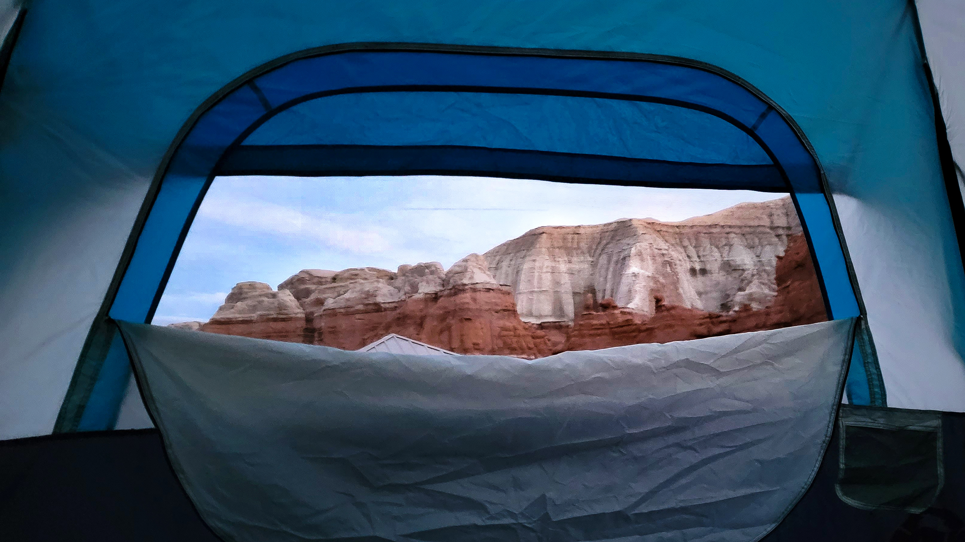 Looking out through the opening of a blue tent toward layered desert cliffs